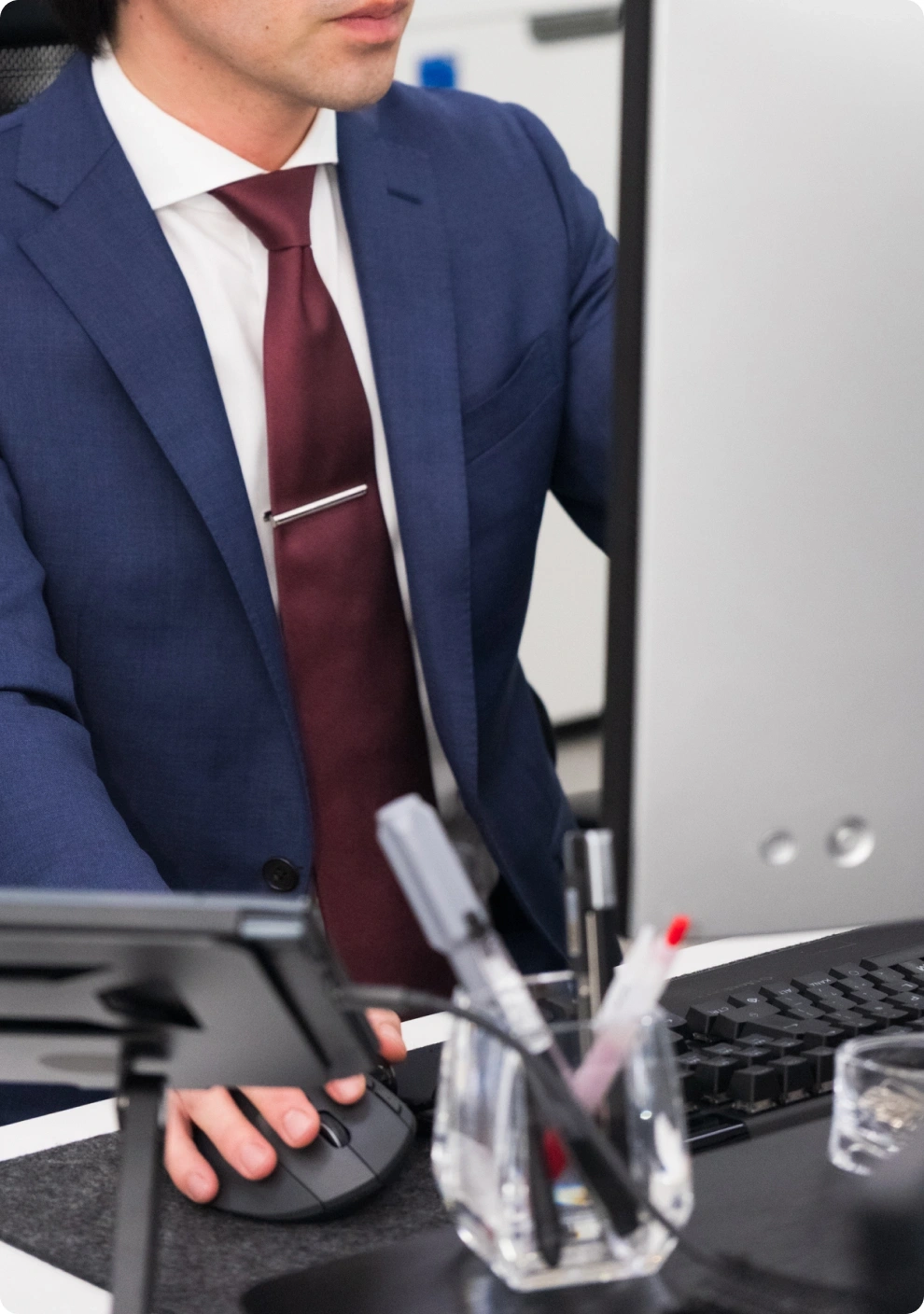 デスクでマウスを操作しモニターに向かうスーツ姿のスタッフ