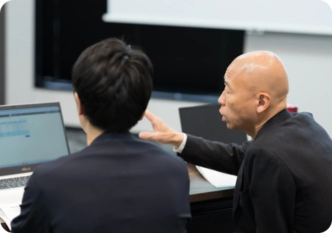 ベテランスタッフが画面を指さしながら後輩に説明している様子