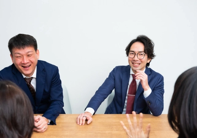 2人のスタッフがテーブルを挟んで笑顔で会話している様子