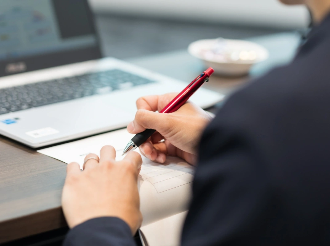 ノートPCの前でペンを持ち書類に記入しているクローズアップ